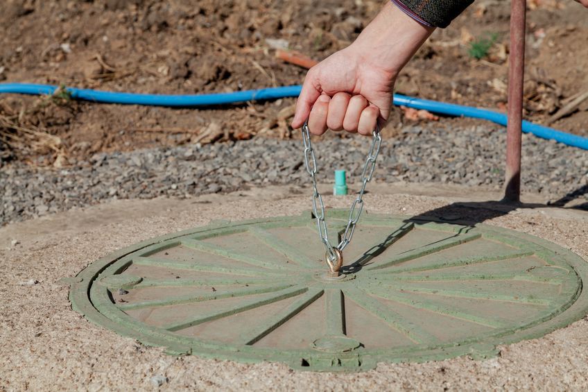 Hand pulling chain on septic tank to perform an inspection